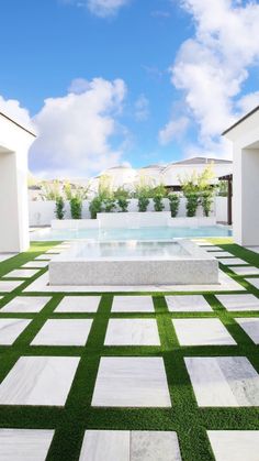 an outdoor swimming pool surrounded by grass and white tiles with blue sky in the background