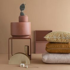 a stack of pillows and other decorative items on a pink surface with a cactus in the background