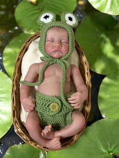 a newborn baby wearing a frog hat and diaper in a basket with lily pads