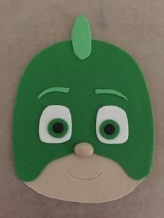 a green mask with eyes and nose on top of a cardboard board that has been cut out to look like a face