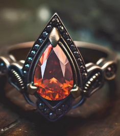 a ring with an orange stone in the center on top of a wooden table,