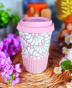 a pink coffee cup sitting on top of a wicker basket next to purple flowers