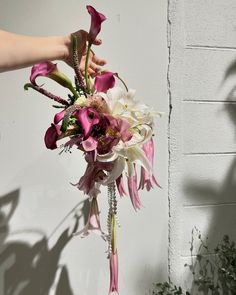 a bouquet of flowers is being held up by someone's hand against a white wall