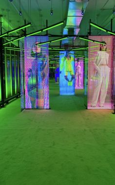 an art installation in a building with multiple colored screens on the walls and people walking through it