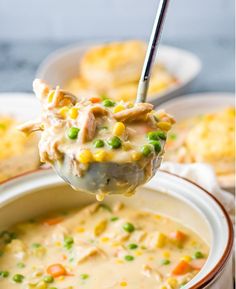 a ladle full of chicken pot pie soup with peas and corn on the side