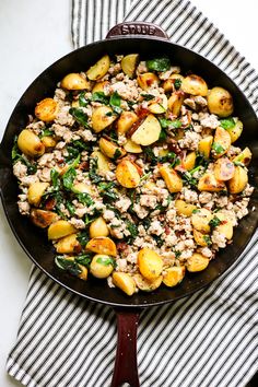 a skillet filled with potatoes, meat and spinach on top of a striped cloth