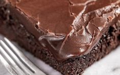 a close up of a piece of chocolate cake on a plate with a knife and fork