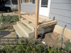 a house with steps leading up to the front door and back porch area, next to a garden hose