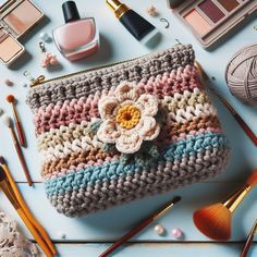 a crocheted purse sitting on top of a table next to makeup and brushes