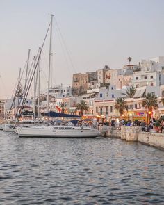 several sailboats are docked in the water near some buildings and people walking on the sidewalk