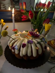 a bundt cake decorated with white icing and flowers on a table next to a lit candle