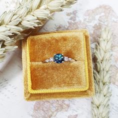 an engagement ring in a velvet box on top of a piece of paper next to some flowers