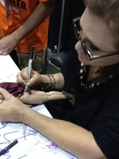 two people sitting at a table writing on paper with marker pens and pencils in their hands