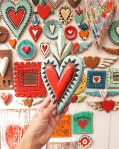 a person holding up a heart shaped object in front of a wall full of hearts