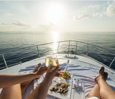 two people toasting while sitting on a boat in the ocean with food and drinks