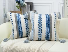 two blue and white pillows sitting on top of a couch next to a vase with flowers