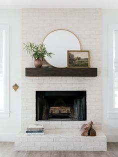 a white brick fireplace with a mirror and potted plant on the mantel above it