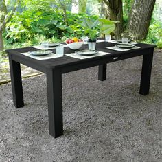 a table with plates and bowls on it in the middle of a gravel area next to trees