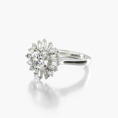 an engagement ring with a center diamond surrounded by small round brilliant cut diamonds, on a white background