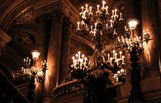 an ornate chandelier with many candles lit up in the dark, surrounded by pillars