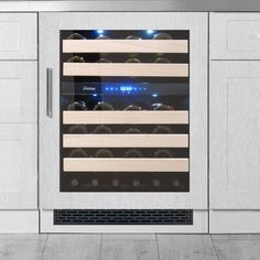 a wine cooler in the middle of a kitchen with white cupboards and drawers on both sides