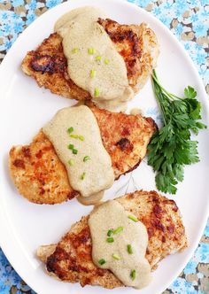 three pieces of chicken covered in gravy on a white plate with parsley