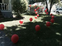 many red balloons are floating in the air near some trees and grass on a lawn