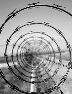 barbed wire is in the middle of an open field with a road and blue sky behind it