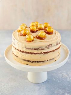 a cake with frosting and nuts on top sitting on a white plate in front of a wall