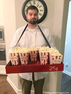 a man is holding a tray with popcorn and a clock on the wall behind him