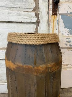 an old wooden barrel with rope on the top sitting in front of a white door