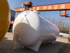 a large white tank sitting on top of a cement slab next to an orange crane