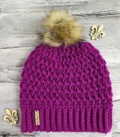 a purple knitted hat with a pom - pom on top and gold buttons