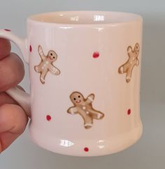 a hand holding a white coffee mug with gingerbreads on it and red polka dots