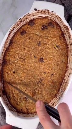 a person cutting into a baked dessert in a white dish with chocolate chips on top