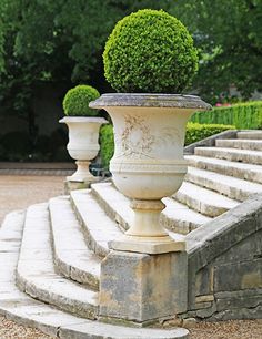 two large white vases sitting on top of stone steps next to trees and bushes