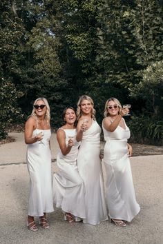 three women in white dresses are posing for a photo with wine glasses on their hands