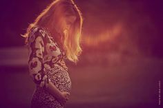 a pregnant woman is looking down at her cell phone while standing in the sun light