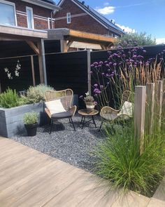 two chairs sitting on top of a wooden deck next to a planter filled with purple flowers