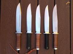 five knives are lined up in a row on a wooden surface with one knife stuck to the wall