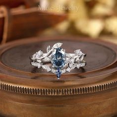 a blue and white diamond ring sitting on top of a wooden box with other jewelry items in the background