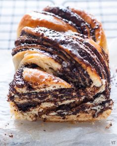 a pastry with chocolate and powdered sugar swirls on it's side, sitting on top of wax paper