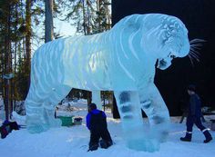 two people are standing next to an ice sculpture of a large tiger in the snow