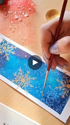 someone is painting snowflakes on a card with watercolors and pencils