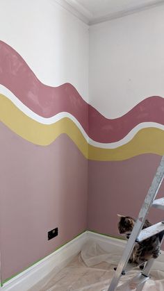 a cat sitting on a step ladder in front of a wall painted with pink and yellow stripes