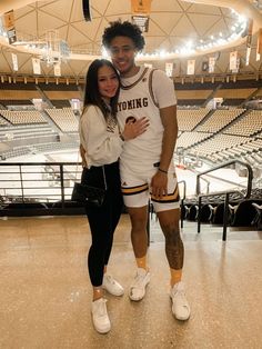 a man standing next to a woman in front of a basketball court