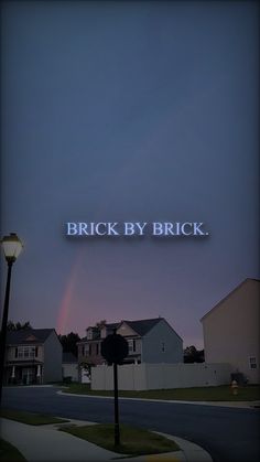 the word brick by brick is lit up at night in front of a row of houses