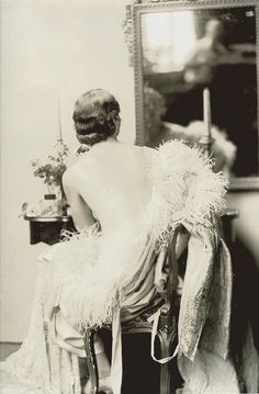 an old fashion photo of a woman sitting in a chair with feathers on her back