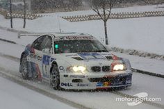 a white car driving down a snow covered road in the middle of winter with headlights on