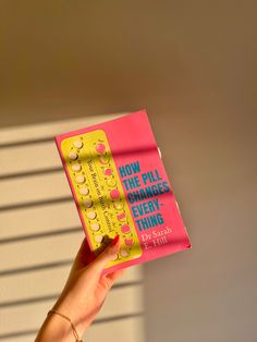 a person holding up a pink book in front of a white wall